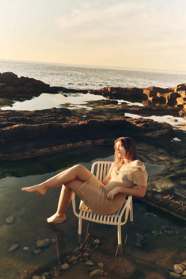 Nicole Wallace sitting barefoot on an outdoor chair beside the sea.