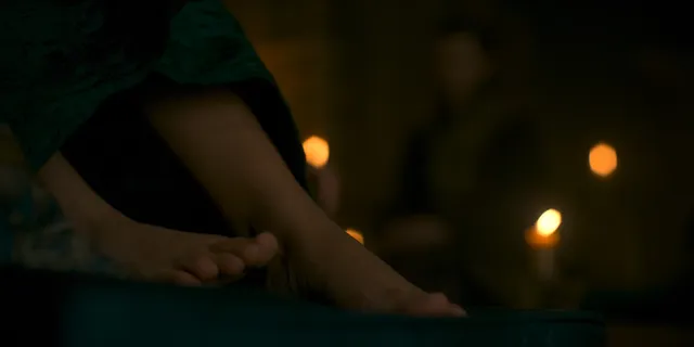 Olivia Cooke resting her feet beside candles in a screen scene.