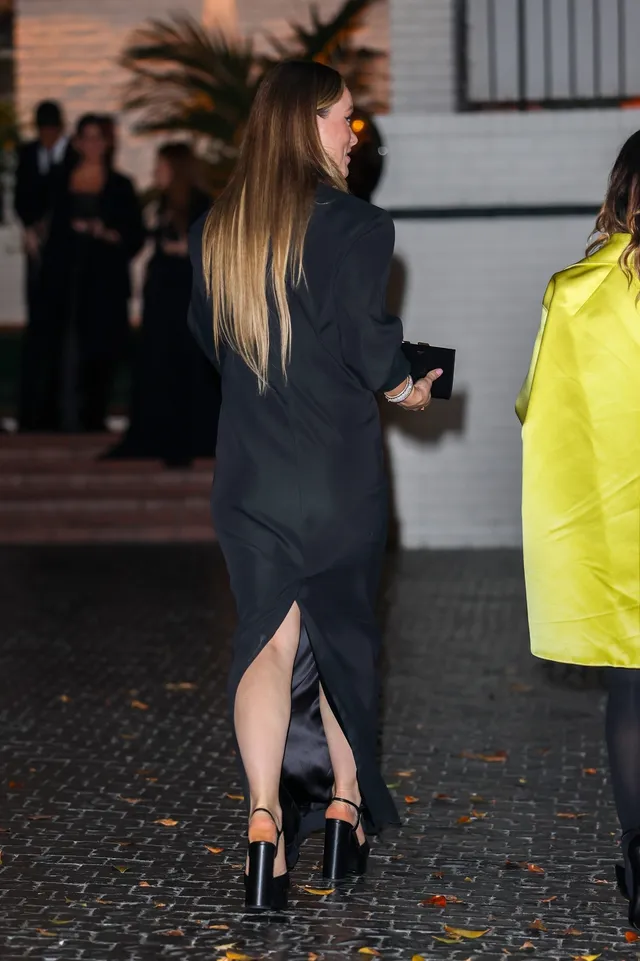 Olivia Wilde walking outdoors in a black dress and high heels.