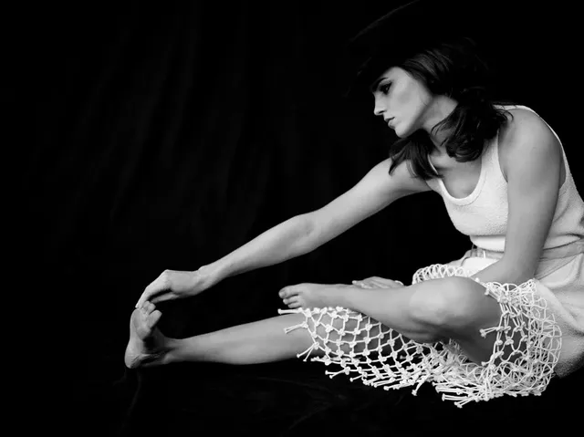 Emma Watson: seated barefoot in a black-and-white studio portrait.