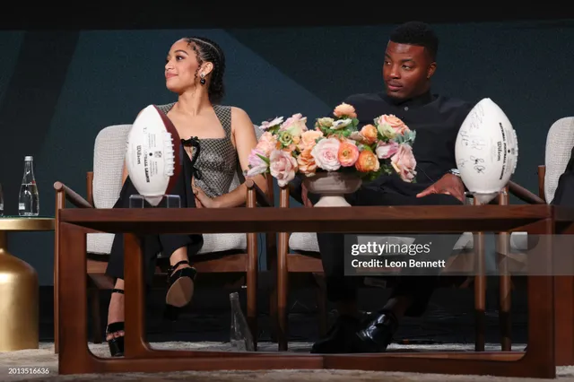 Samantha Logan sitting onstage in a dark outfit and black platform heels.