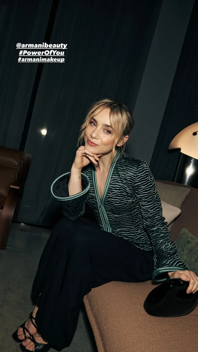Clara Galle sitting on a sofa in a patterned jacket, dark skirt and lace-up heels.