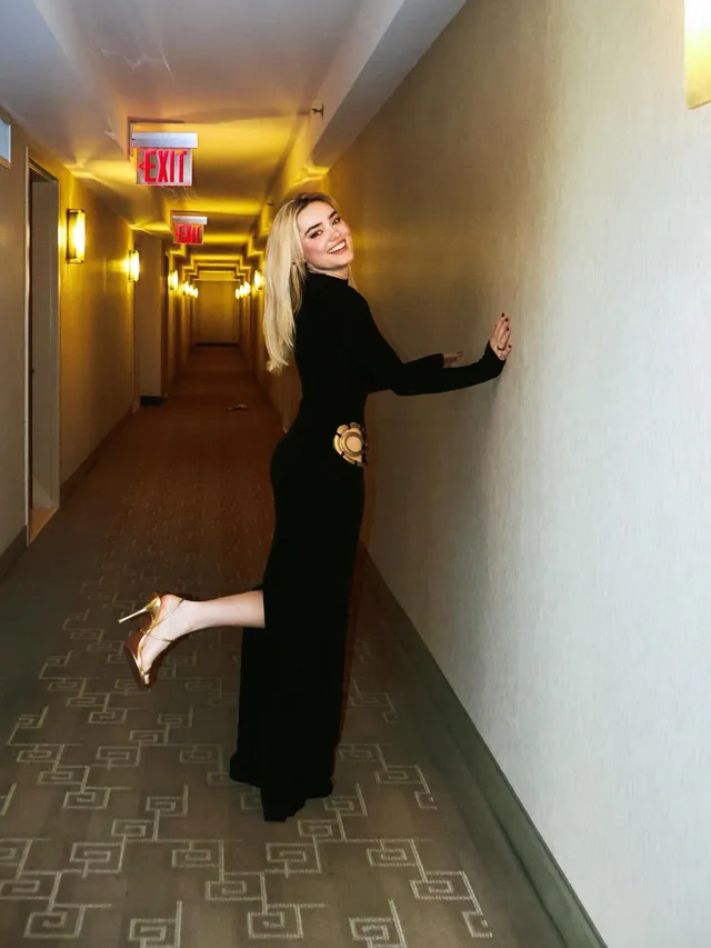 Meg Donnelly posing in a corridor in a long black outfit and flat sandals.