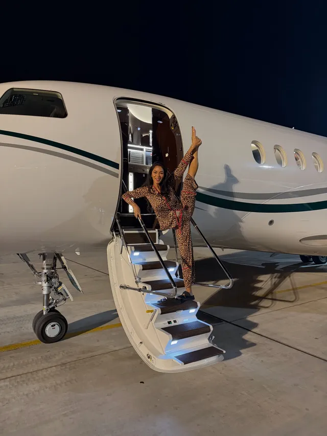 Nicole Scherzinger stretching barefoot beside an aircraft doorway.