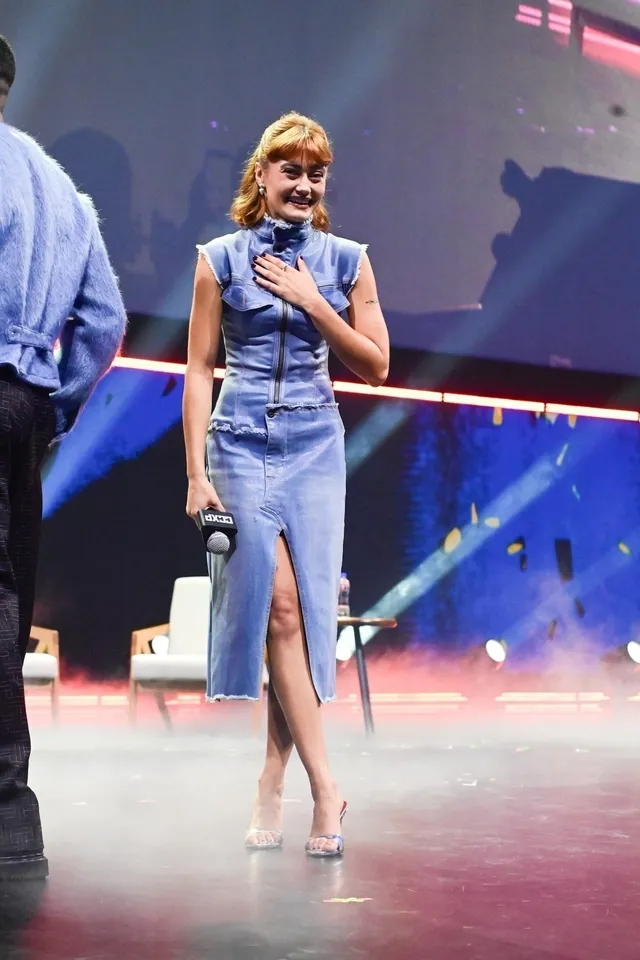 Ella Purnell standing onstage with a microphone in a blue dress.