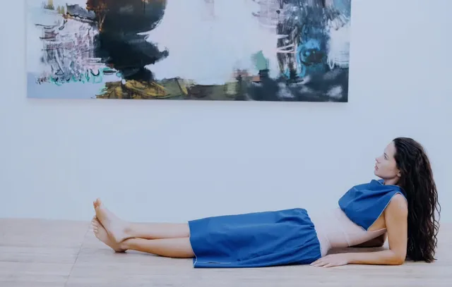 Adriana Lima reclining barefoot in a blue dress against a pale backdrop.