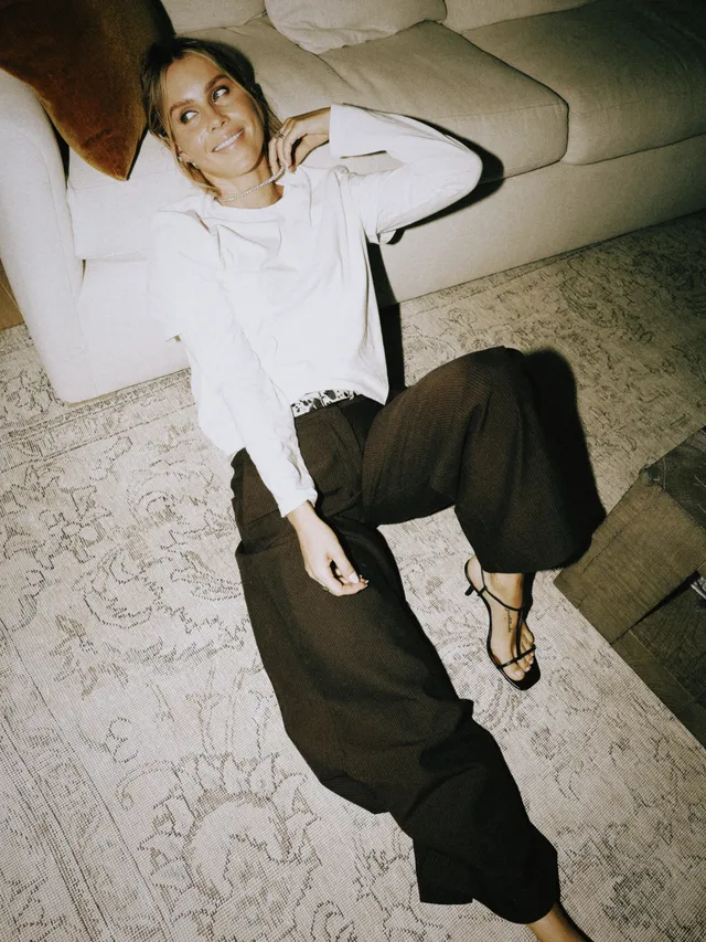 Claire Holt reclining on a sofa in a black-and-white outfit.