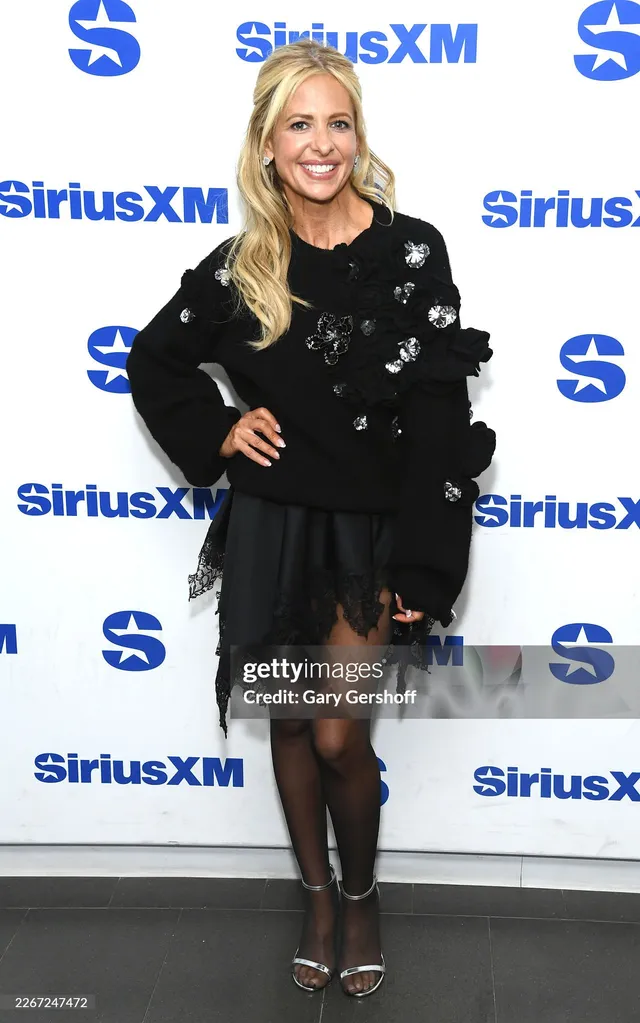 Sarah Michelle Gellar standing at an event in a black outfit and strappy heels.