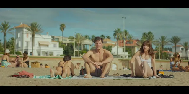 Úrsula Corberó sitting barefoot with a group on a beach in a scene.