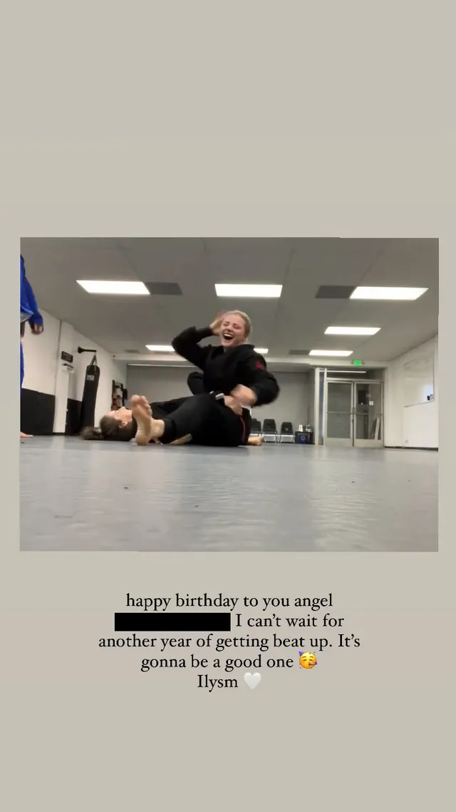Chloë Grace Moretz sitting barefoot beside another person on a gym floor.