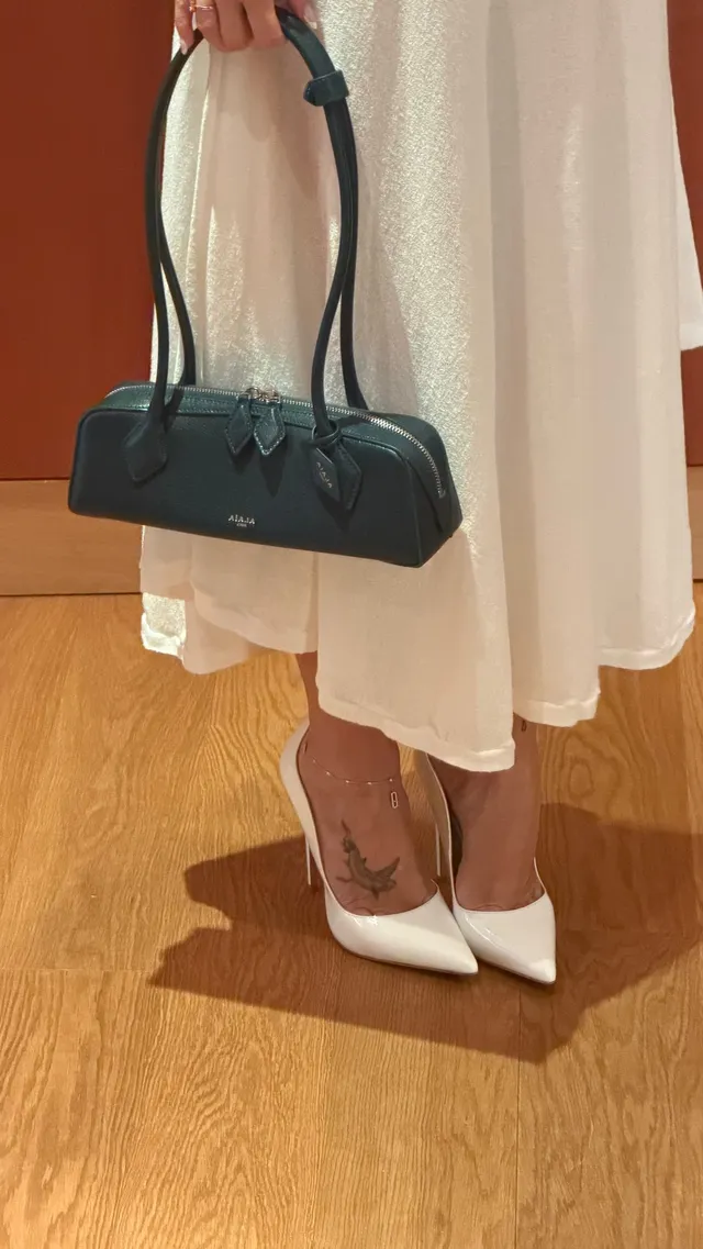 Ester Expósito showing white pointed heels beneath a pale skirt while holding a handbag.