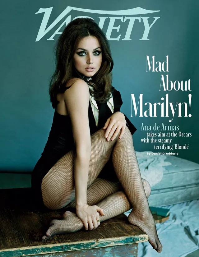 Ana de Armas seated barefoot in a black dress for a magazine cover.