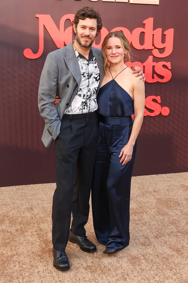 Kristen Bell posing beside another guest in a long blue outfit at a premiere.