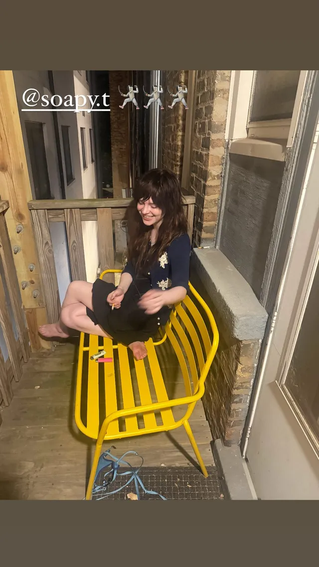 Sophie Thatcher sitting barefoot on a yellow bench outdoors.