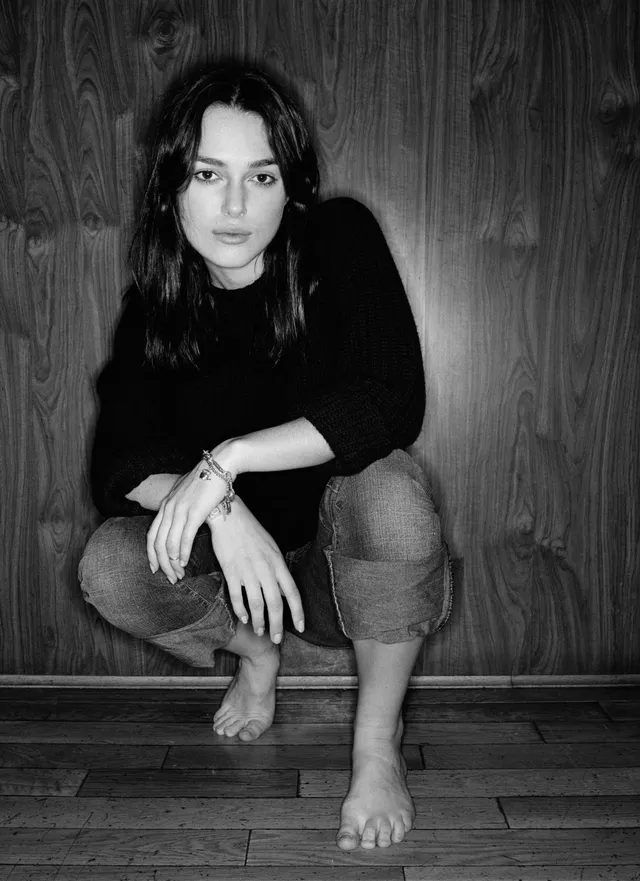 Keira Knightley a monochrome portrait seated against a wooden wall.