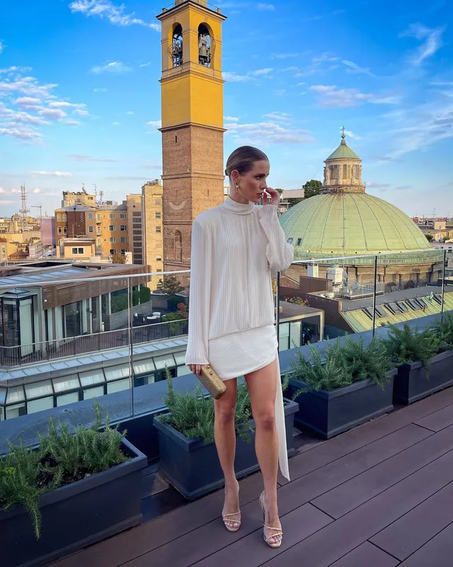Claire Holt posing on a rooftop terrace in a pale shirt dress.
