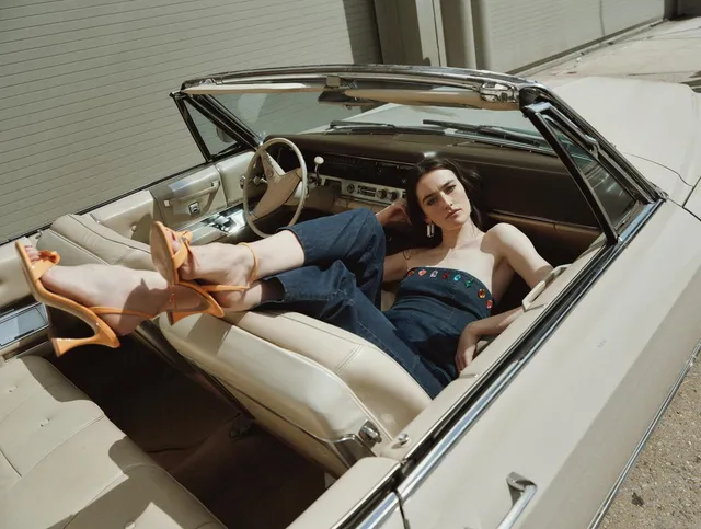 Sarah Pidgeon reclining in a convertible wearing a denim outfit and tan shoes.