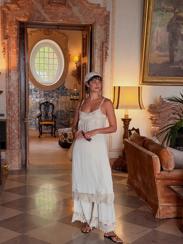 Taylor Hill wearing flat sandals with a long white dress in an ornate room.