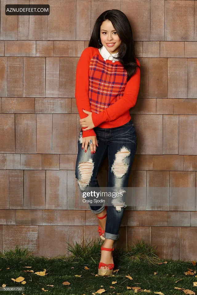 Cierra Ramirez in a red striped top, cropped jeans and ankle-strap heels beside a brick wall.