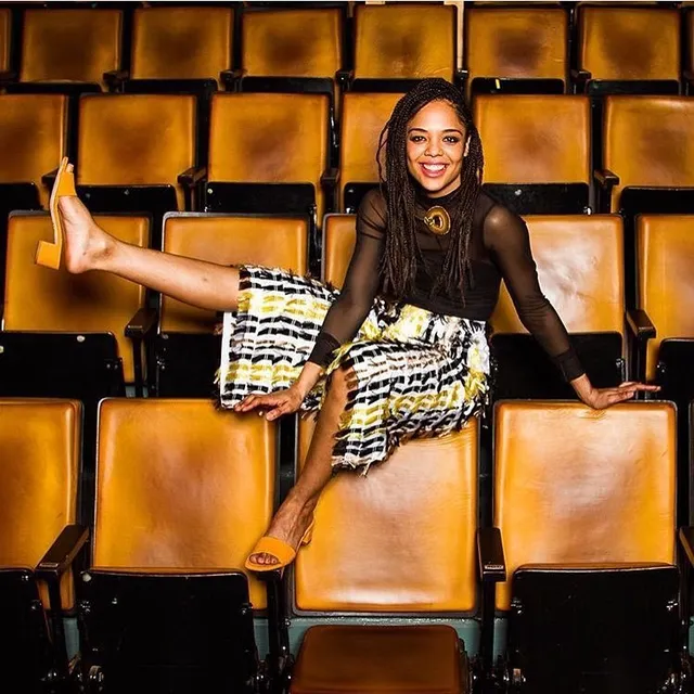 Tessa Thompson sitting across cinema seats in a patterned skirt.