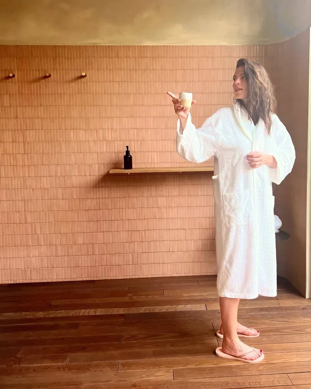 Hayley Atwell standing in a robe and flat slippers in a tiled room.