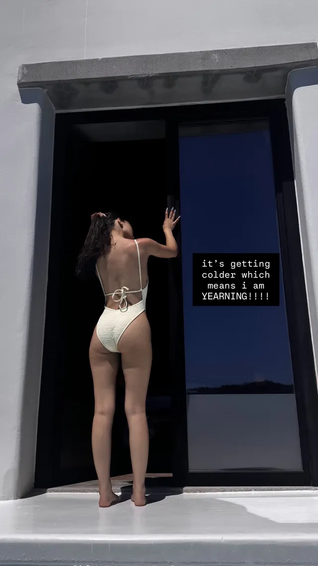 Rachel Zegler standing barefoot in a swimsuit beside a doorway.