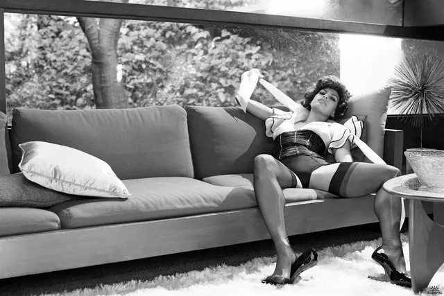 Eva Mendes reclining on a sofa in a monochrome fashion portrait.