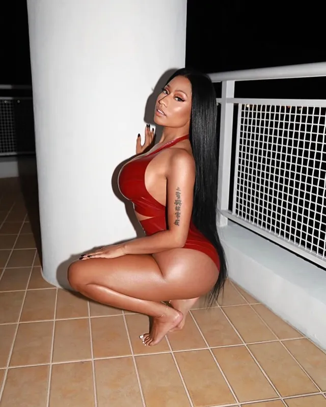 Nicki Minaj crouching barefoot on a tiled balcony.
