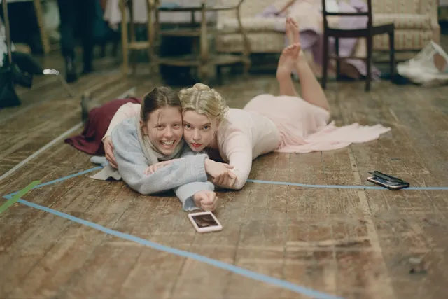 Anya Taylor-Joy lying on the grass in a pale pink dress with her bare feet raised.