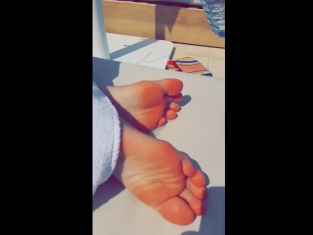 Kendall Jenner showing bare soles beside a poolside table.