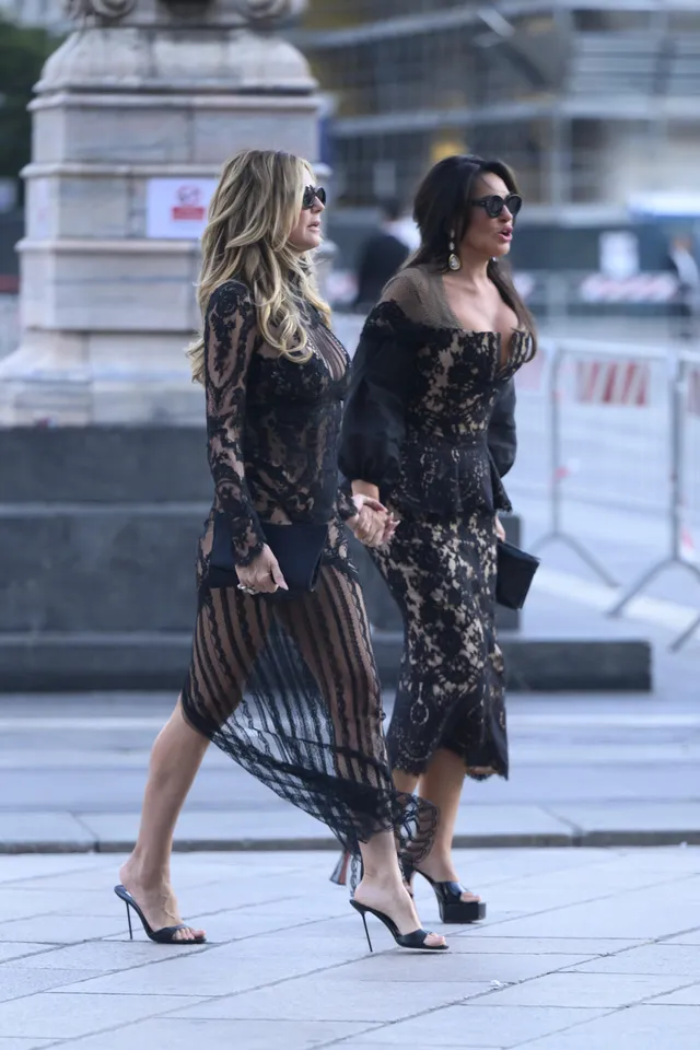 Heidi Klum walking beside a companion in a black lace gown and heels.