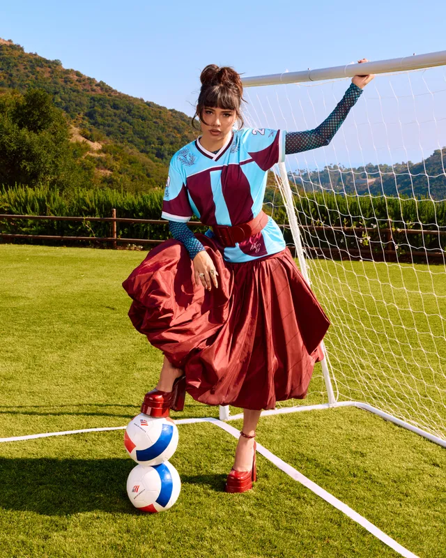 Xochitl Gomez posing beside a sports net in a patterned outfit and heels.