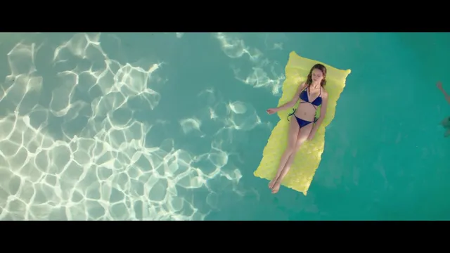 Halston Sage floating barefoot on a yellow pool lounger in a scene.