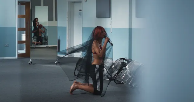 Naomi Scott kneeling barefoot in a rehearsal room with floor fans.