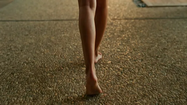 Dakota Johnson standing barefoot on a rug in warm light.