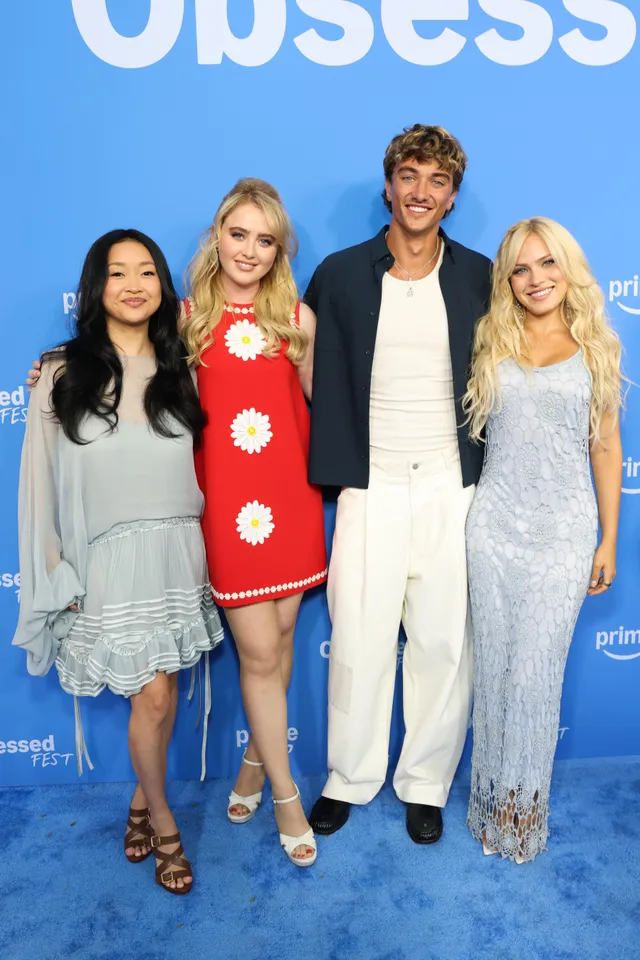 Kathryn Newton posing with a group in a red dress and heeled sandals.
