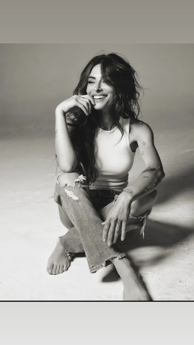 Sarah Shahi sitting for a black-and-white portrait in jeans.