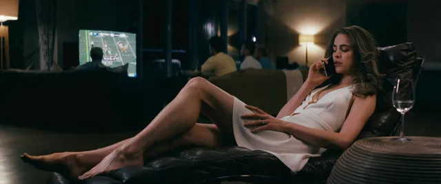 Margaret Qualley a reclining screen scene on a dark sofa.