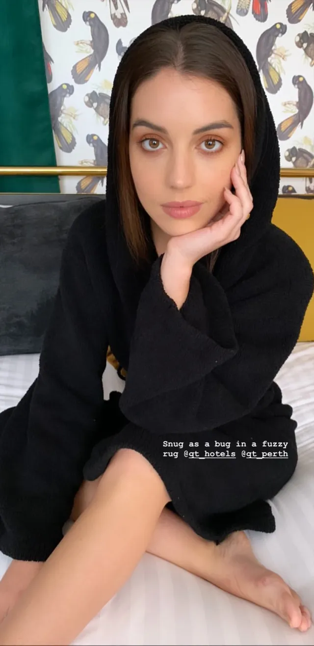 Adelaide Kane sitting cross-legged in a dark casual outfit.