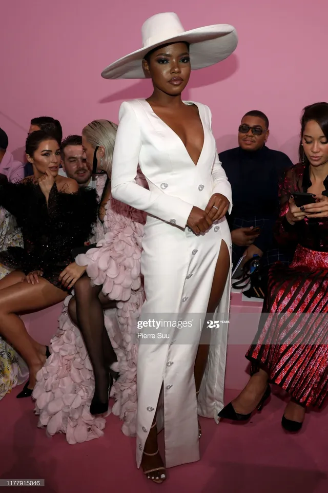 Ryan Destiny posing in a white suit, wide-brimmed hat and strappy heels.