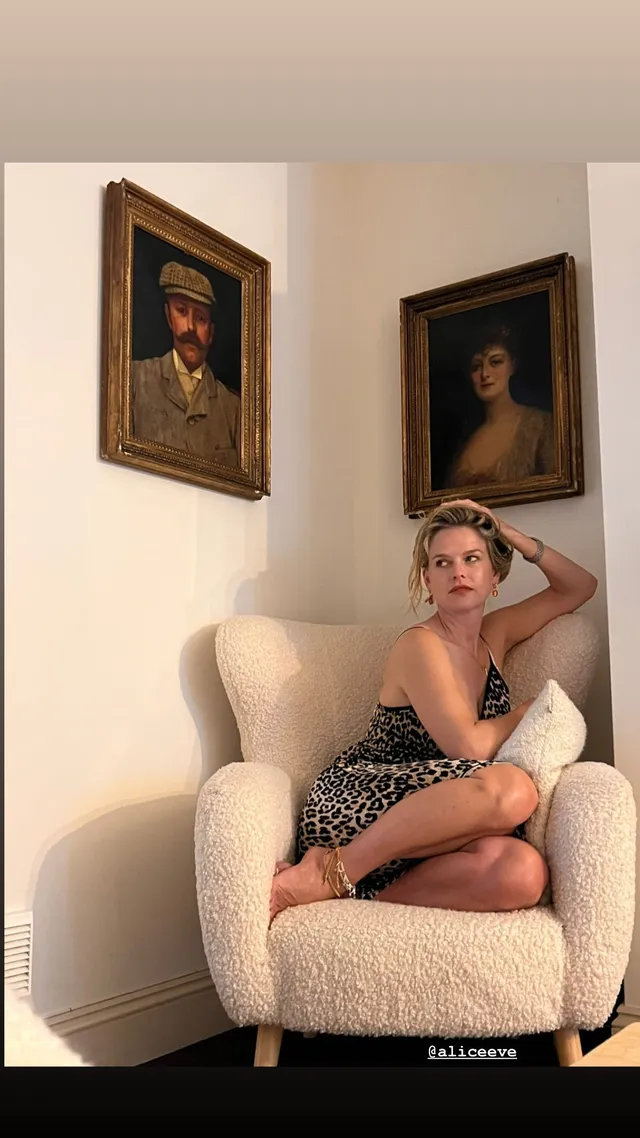Alice Eve sitting cross legged in a pale armchair.