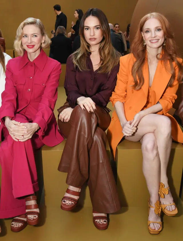 Jessica Chastain sitting with other guests in an orange jacket and platform sandals.