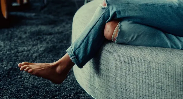 Sienna Miller resting bare feet on an armchair in a screen scene.