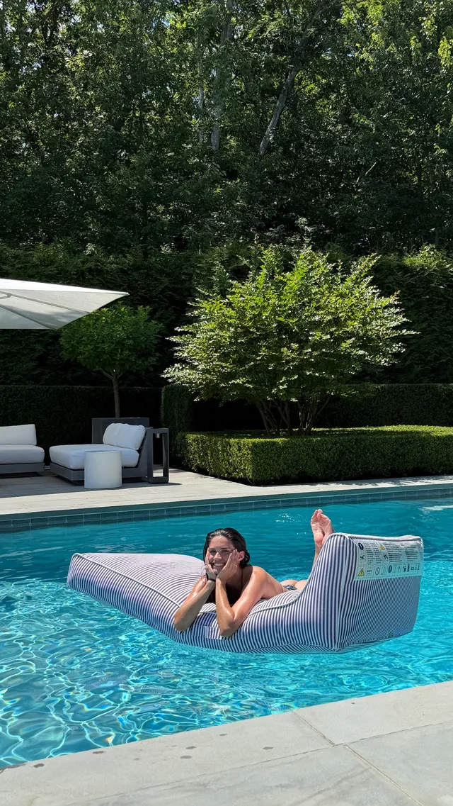Sara Sampaio relaxing on a floating pool lounger with her bare feet raised.