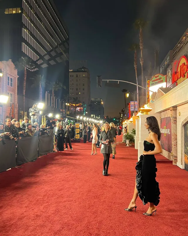 Greta Onieogou standing on a red carpet in a black dress and pointed heels.