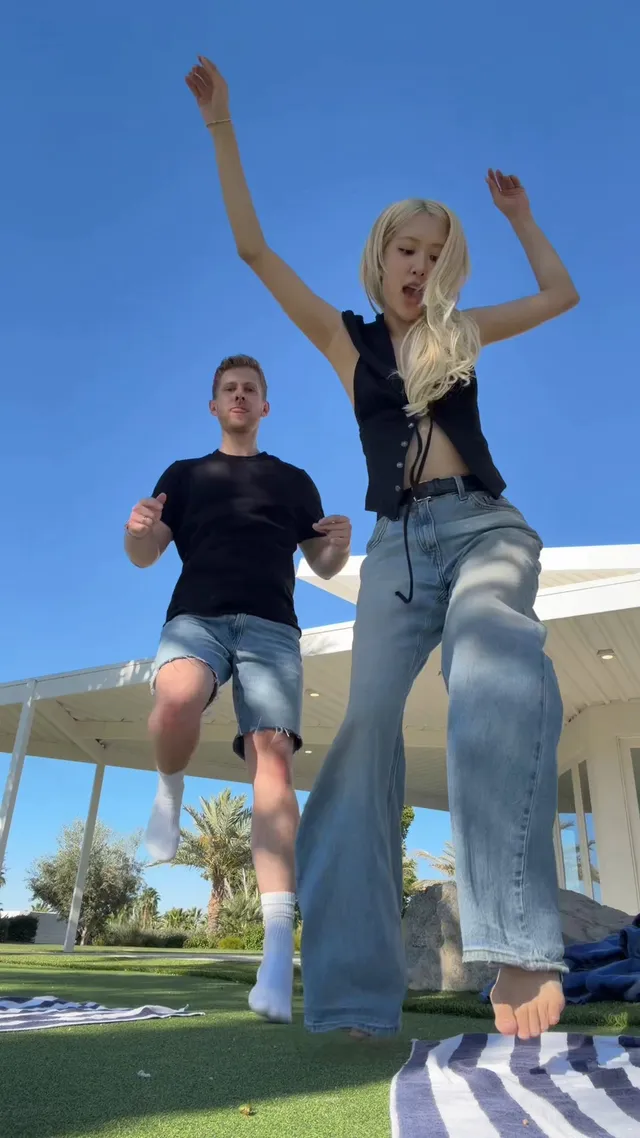 Rosé dancing barefoot beside a striped towel on a lawn.