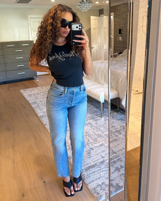 Madison Pettis taking a mirror selfie in a dark top, blue jeans and flat sandals.