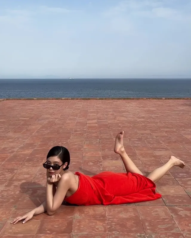 Jennie Kim lying on a terrace in a red outfit with her bare feet raised.