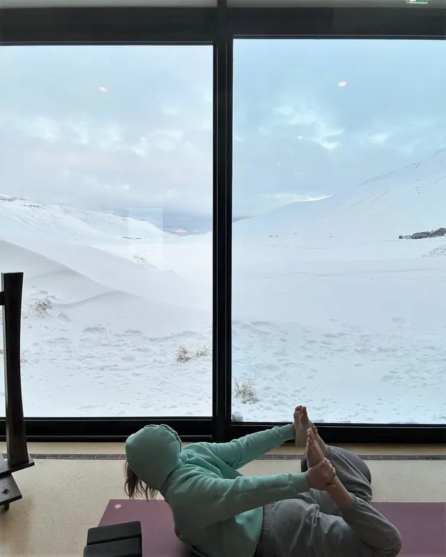 Alexandra Daddario reclining near an ocean-view window with her bare feet raised.