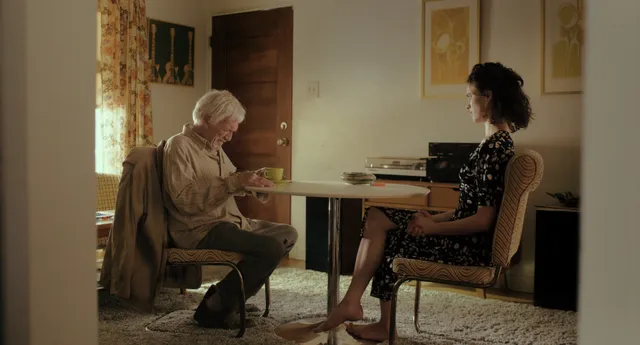 Margaret Qualley a seated screen scene beside another character.